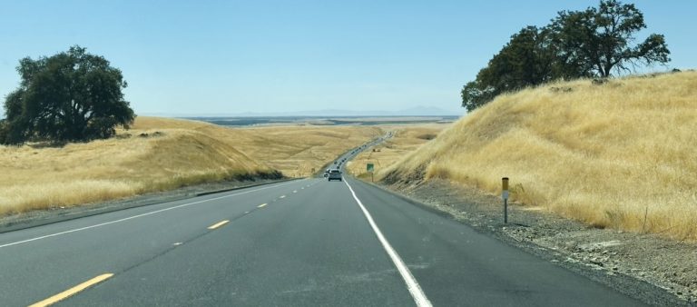 Highway road trip through California with golden hills and tree-lined scenery