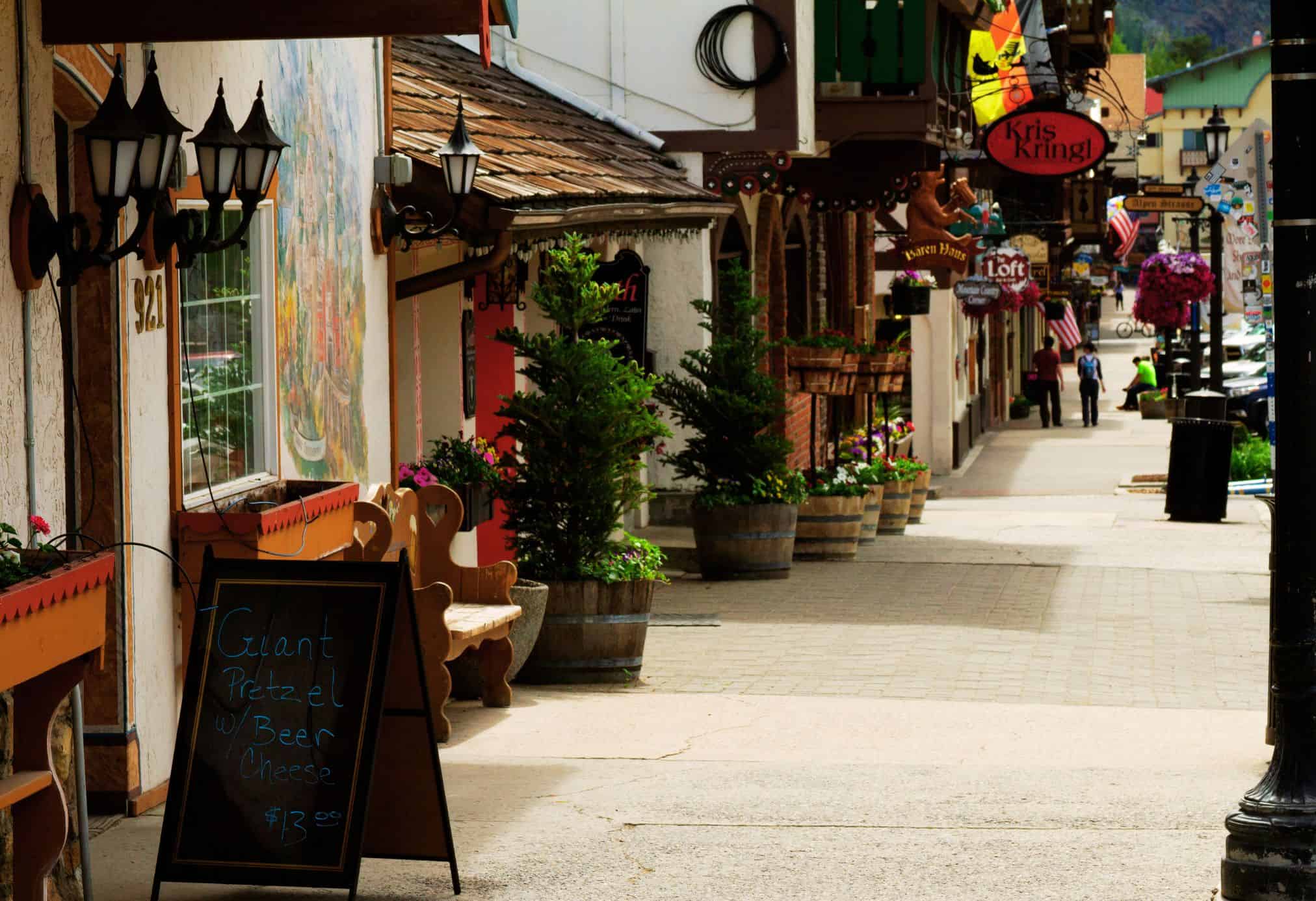 Charming Bavarian-style shops and restaurants along Front Street in Leavenworth, Washington, with murals, flower boxes, and a sign for giant pretzels and beer cheese