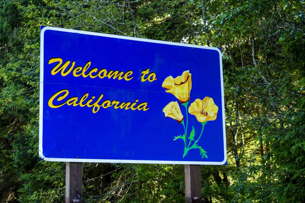 California welcomes you sign at the state border with bright yellow poppies and blue sky in the background
