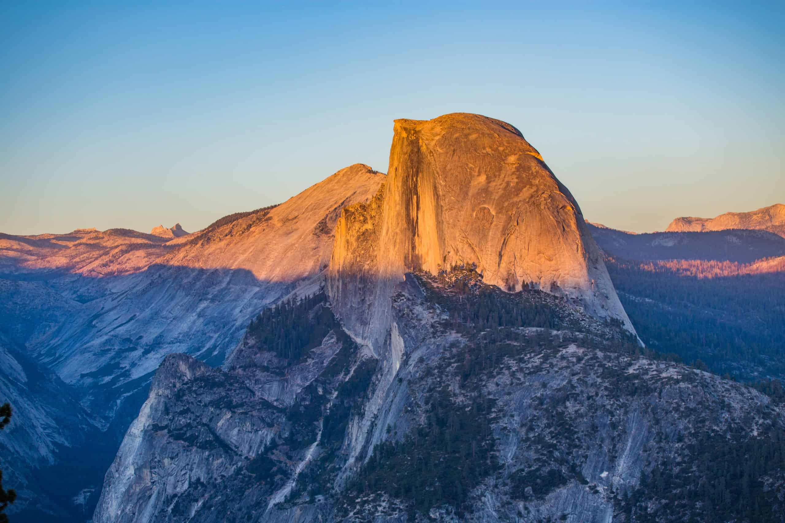 Golden hour view of Half Dome in Yosemite National Park with warm sunlight casting dramatic shadows on granite cliffs
