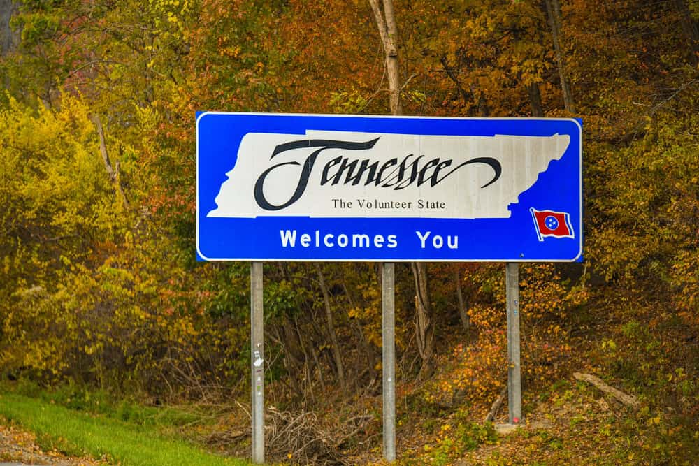 Welcome to Tennessee blue roadside sign with musical notes and the state flag emblem, set against a sunny sky or green highway backdrop