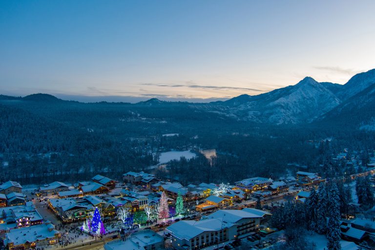 Aerial view of Leavenworth, Washington at Christmas, glowing with holiday lights beneath snow-covered Cascade Mountains