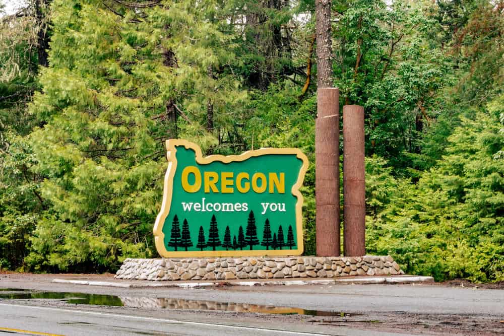 Oregon welcomes you green roadside sign at the state border surrounded by lush trees