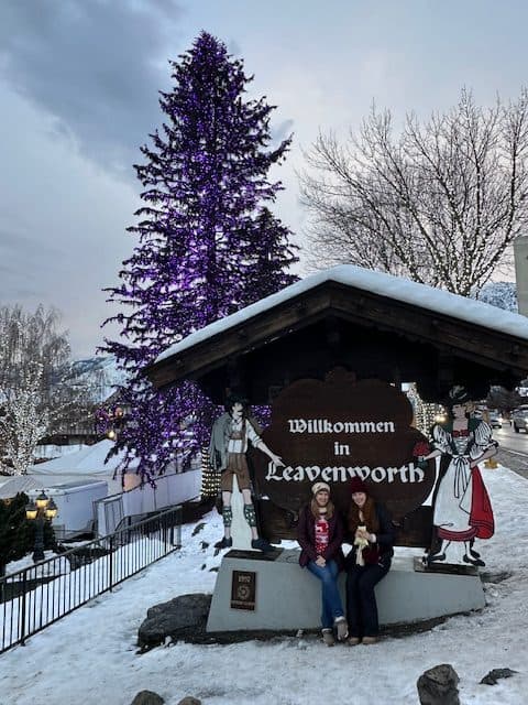 Two women sitting on the iconic "Willkommen to Leavenworth" welcome sign in Leavenworth, Washington