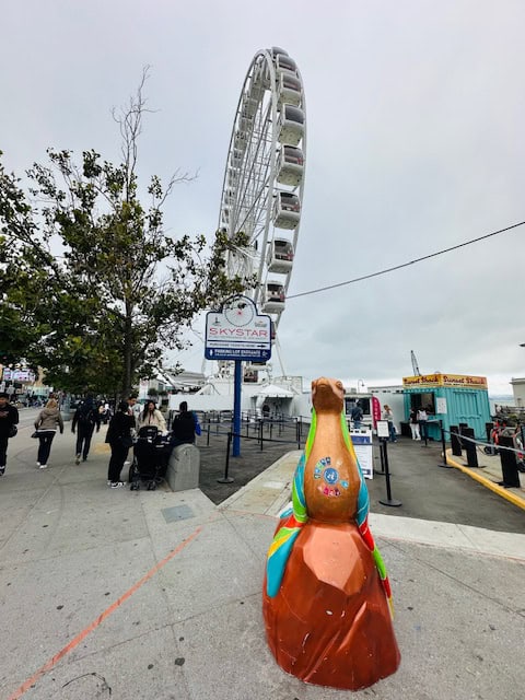 Colorful sea lion statue in front of the SkyStar Wheel at Fisherman’s Wharf, a popular San Francisco attraction that feels safe and family-friendly.