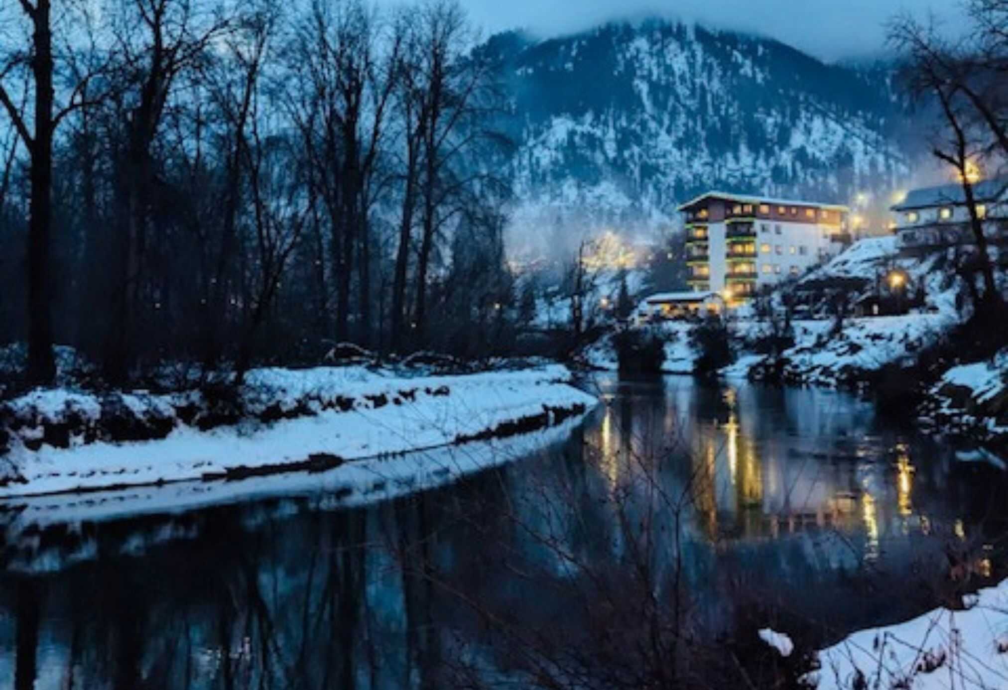 Snowy winter evening in Leavenworth, Washington with river reflections, mountain views, and cozy village lights