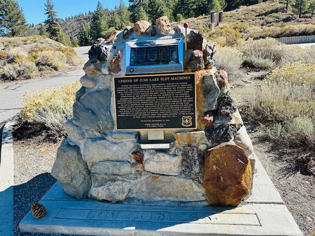 Stone monument in June Lake, California, featuring the “Legend of June Lake Slot Machines” plaque — a quirky historical stop surrounded by fall foliage and mountain scenery