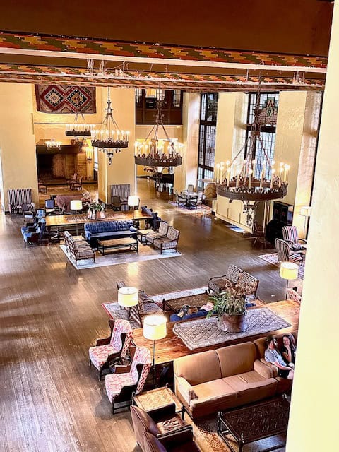 Warm, historic lounge inside The Ahwahnee Hotel in Yosemite National Park, featuring rustic wooden furniture, Navajo-style textiles, grand chandeliers, and tall windows glowing with winter light.