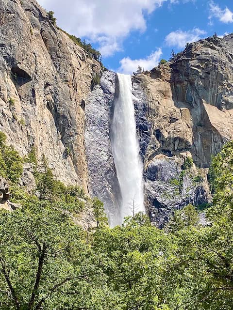 Bridalveil Fall cascading down granite cliffs in Yosemite National Park, surrounded by green trees and blue spring skies