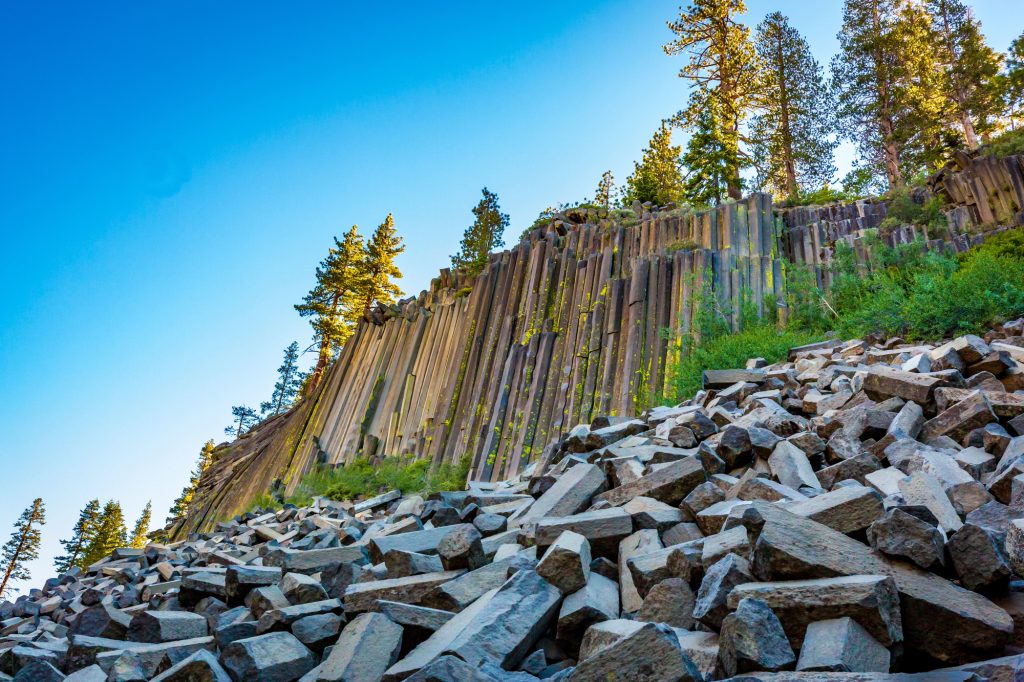 Hexagonal basalt columns at Devil’s Postpile National Monument in Mammoth Lakes, California, surrounded by pine trees and clear blue skies in the Eastern Sierra