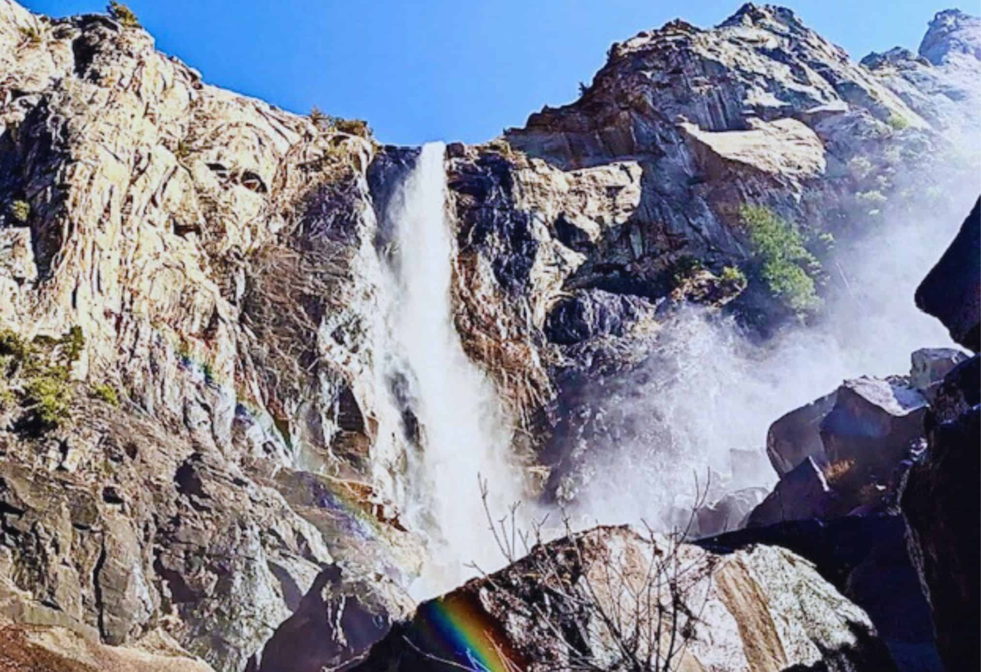 Vernal Fall cascading down granite cliffs in Yosemite National Park, California, with mist and a rainbow forming at the base on a sunny spring day