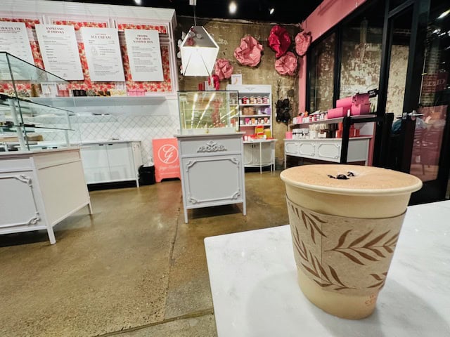 Cup of gourmet hot chocolate at Ginger Elizabeth’s boutique chocolate shop in Sacramento, decorated for Christmas with pink floral displays and festive holiday treats.