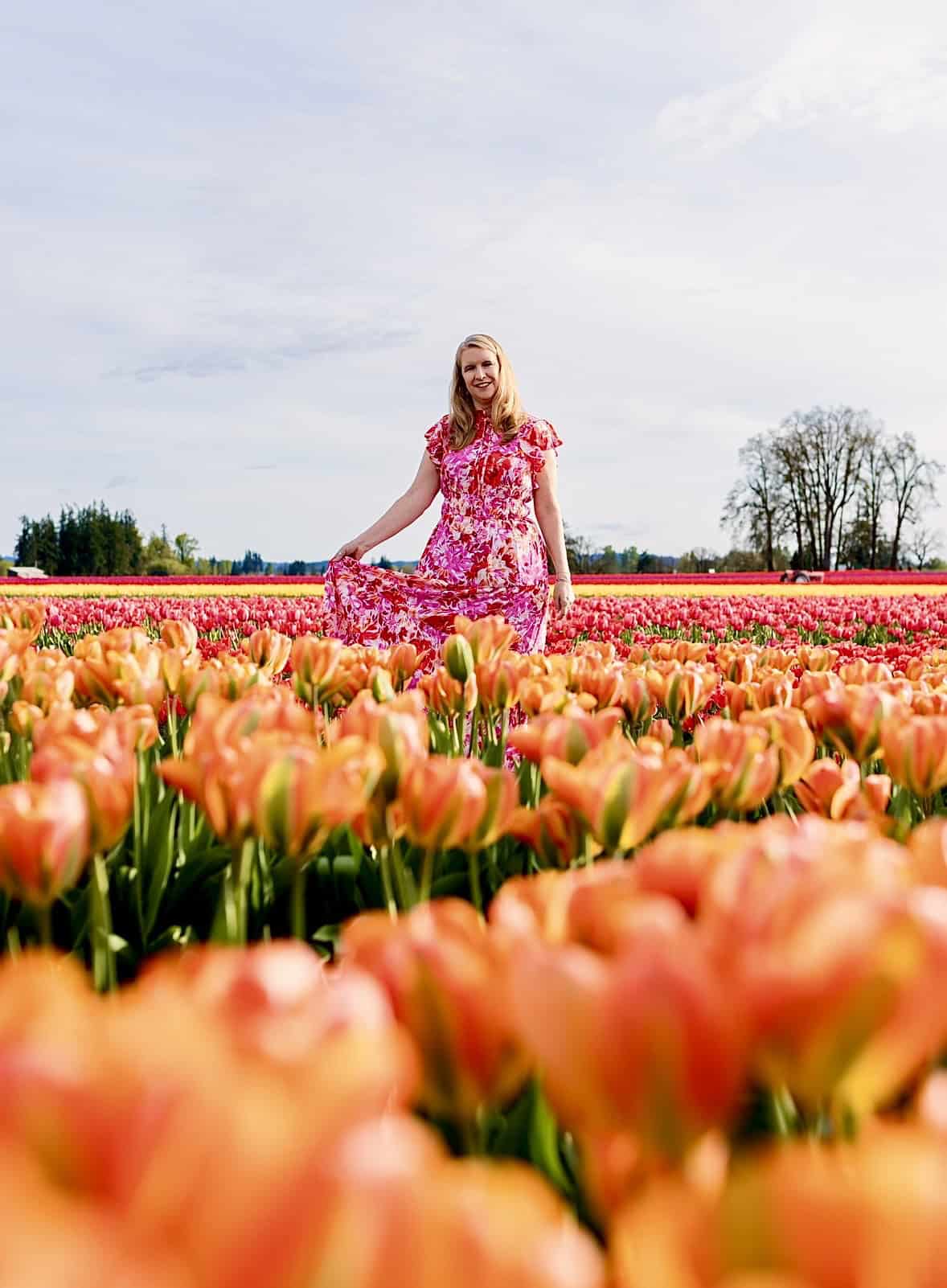 A woman in a pink floral dress walking through bright red tulip fields at the Wooden Shoe Tulip Festival in Oregon on a spring day
