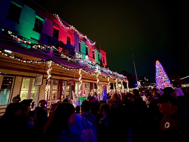 Crowds gather in Old Sacramento for the Theatre of Lights show with historic buildings glowing in red and green Christmas lights and a towering lit holiday tree