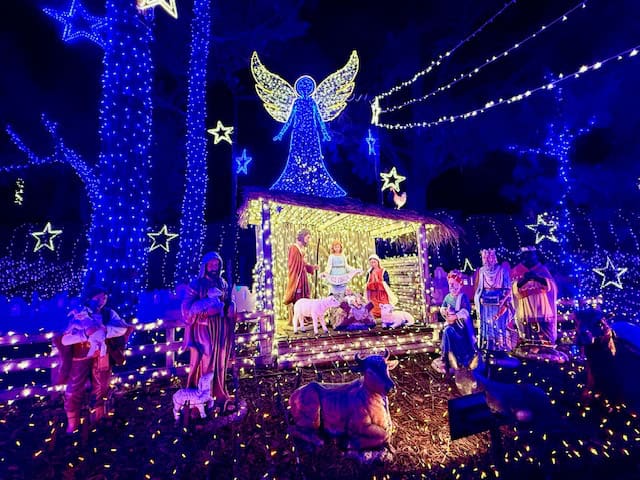 Nativity scene glowing with blue Christmas lights at Cambria Christmas Market, featuring Mary, Joseph, baby Jesus, shepherds, sheep, and an illuminated angel above the manger