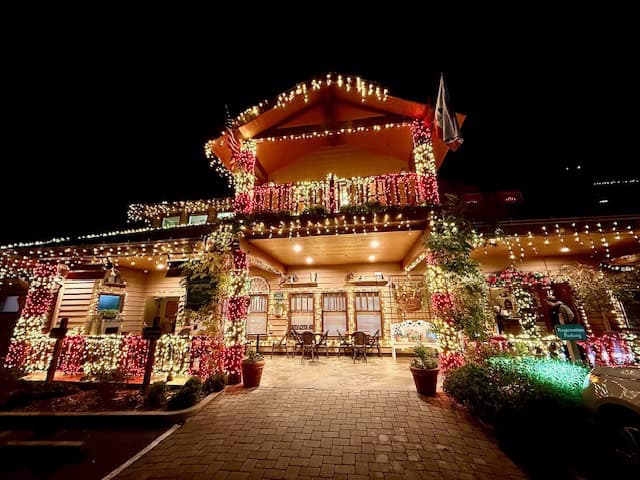 Festively decorated exterior of Cambria Pines Lodge at night, glowing with Christmas lights during the holiday season in Cambria, California