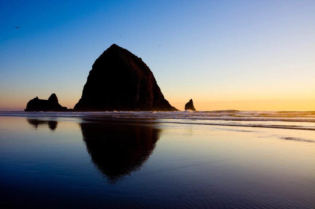 Haystack Rock at Cannon Beach during sunset with ocean waves and reflections on the sand, a popular day trip from Portland, Oregon