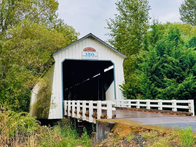 Gallon House Covered Bridge in Silverton, Oregon surrounded by lush greenery and trees on a quiet scenic road