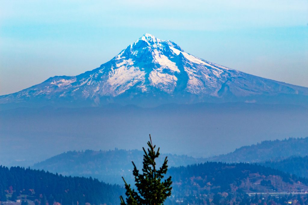 Snow-capped Mount Hood viewed from Pittock Mansion in Portland, Oregon, with layered forested hills in the foreground on a clear day