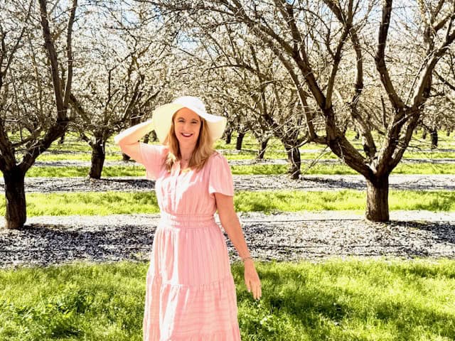 Woman in pink dress standing among blooming almond trees during almond blossom season near Modesto California
