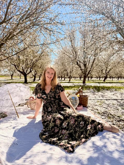 Woman sitting on picnic blanket in blooming almond orchard during spring almond blossom season near Modesto California