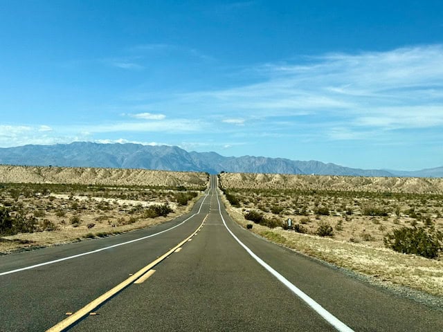 Long desert highway leading through Anza Borrego Desert with mountains in the distance under blue sky