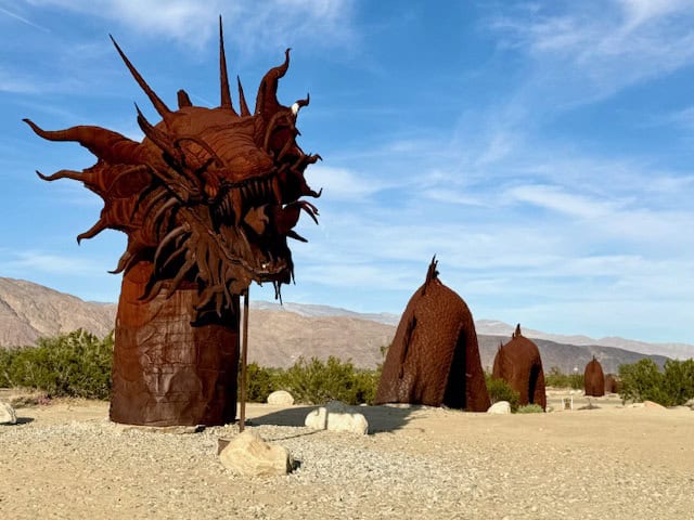 Metal sea serpent sculpture crossing the road in Anza-Borrego Desert at Galleta Meadows with mountains in the background