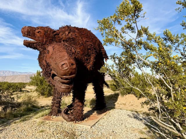 Large metal sloth sculpture in Galleta Meadows in Anza Borrego Desert surrounded by desert plants and blue sky