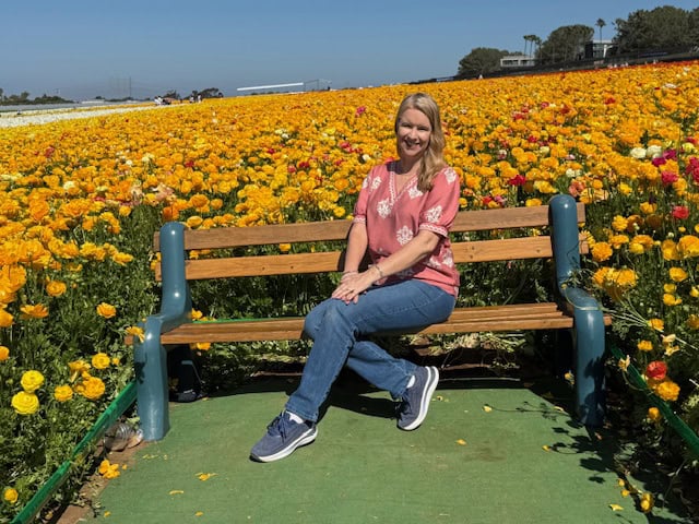 Woman sitting on bench surrounded by vibrant ranunculus flowers at The Flower Fields in Carlsbad California during spring bloom