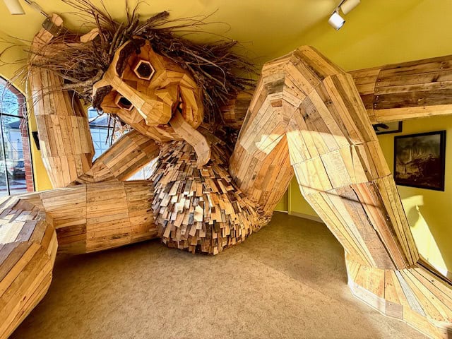 Wooden troll sculpture inside a bright yellow room in Solvang, California, featuring large handcrafted recycled wood art with whimsical expression