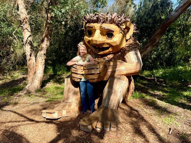 Woman standing inside large wooden troll sculpture made of recycled wood at the South Coast Botanic Garden whimsical outdoor art hidden gem