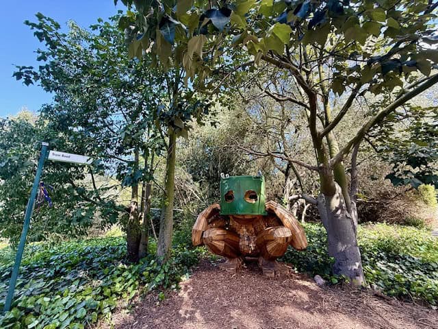 Wooden troll sculpture with green trash can on its head at South Coast Botanic Gardens, whimsical recycled art surrounded by trees