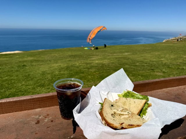 Sandwich and iced drink overlooking the ocean at the Hang Gliderport Cafe in La Jolla, California with a paraglider in the background