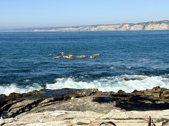 Kayakers paddling along the La Jolla coastline with ocean cliffs and crashing waves in San Diego California