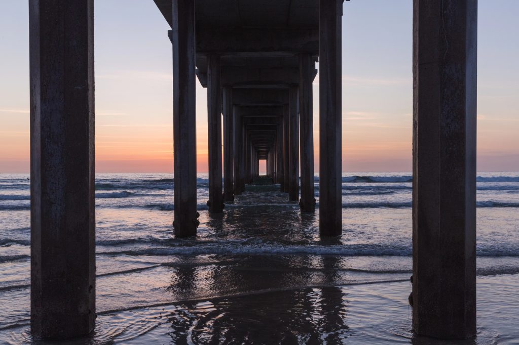 Sunset view beneath Scripps Pier with ocean waves and colorful skies in La Jolla, California