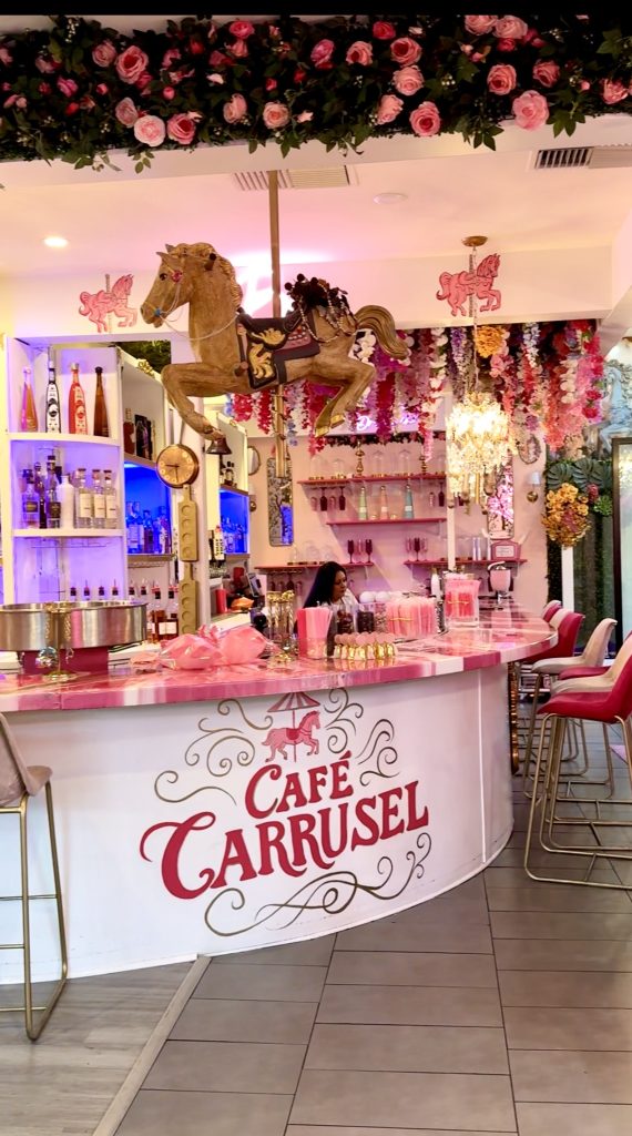 Carousel horse hanging above the pink bar inside Café Carrusel in Santa Rosa, surrounded by roses, chandeliers, and colorful floral décor