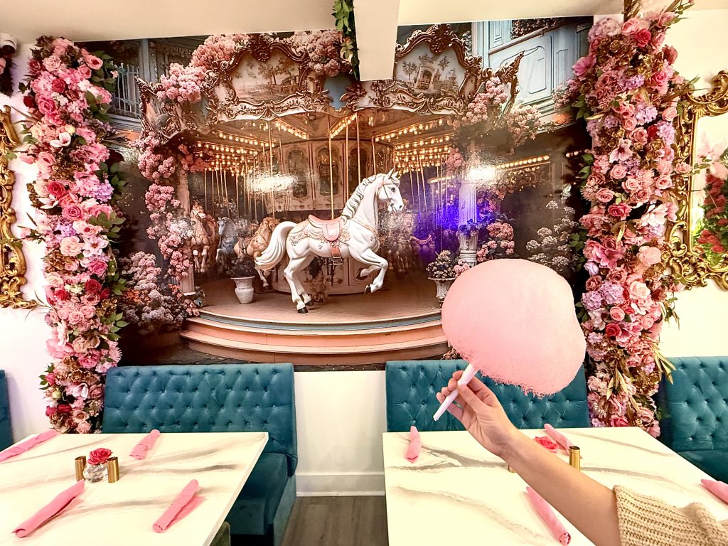 Pink cotton candy inside Café Carrusel in Santa Rosa with a carousel horse mural, pink flowers, and teal seating in the background