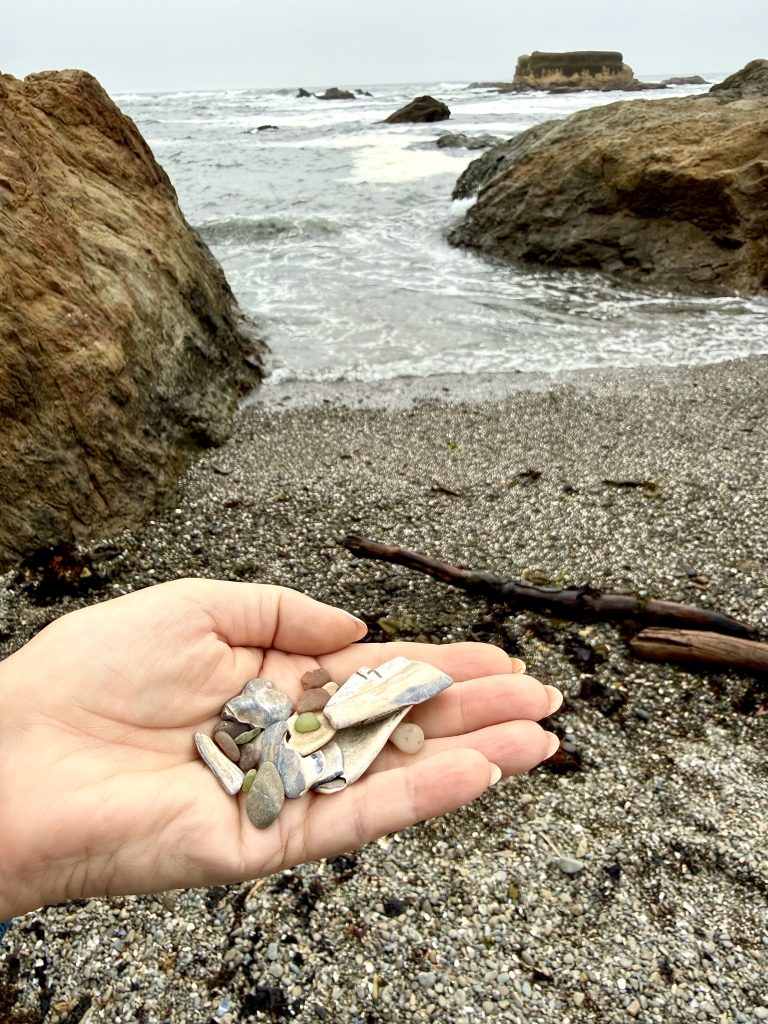 Hand holding colorful sea glass and shells on Glass Beach during a girls weekend in Mendocino, California