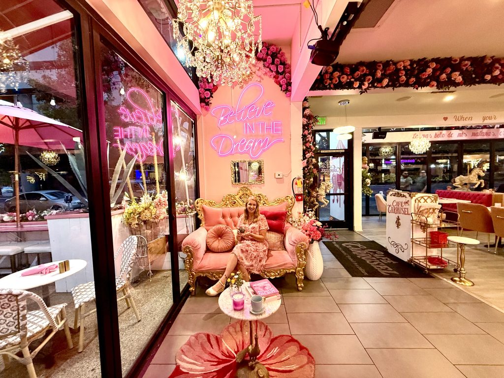 Woman relaxing on a pink velvet sofa inside Café Carrusel in Santa Rosa, surrounded by floral decor, chandeliers, and pink neon lights